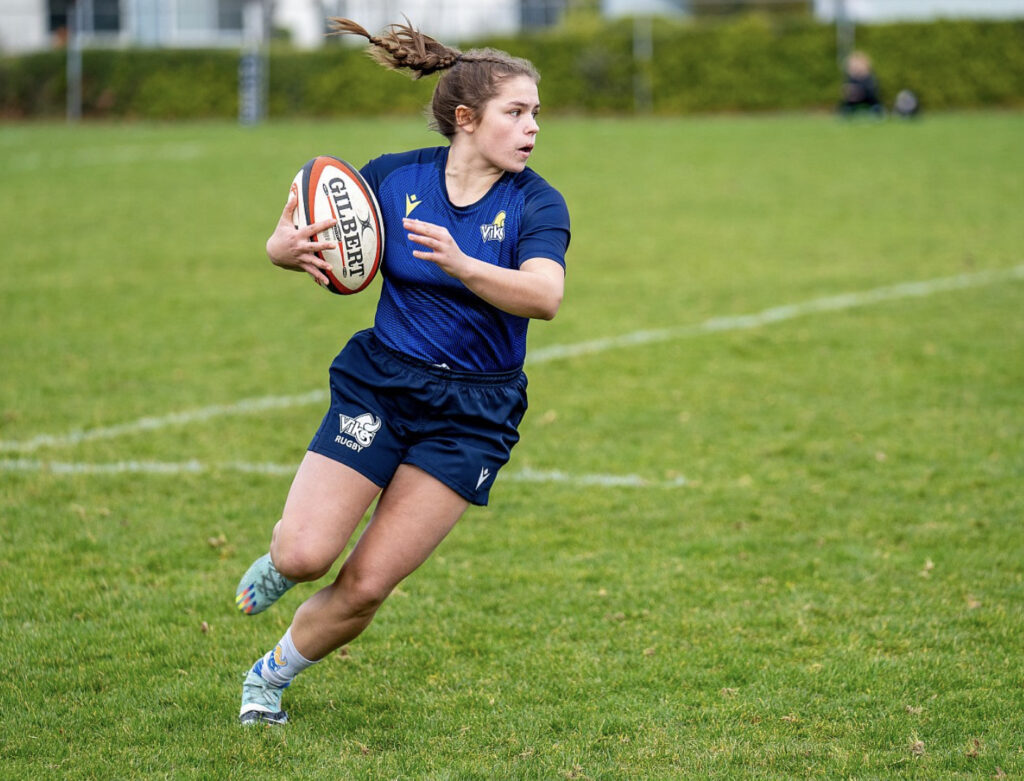 Olivia running down the field holding the rugby ball.