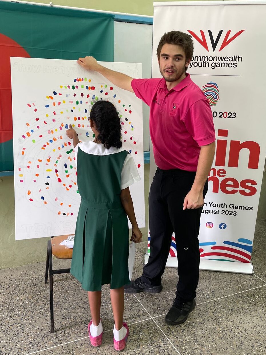 Tyler standing beside a paint board while a child adds a painted thumbprint to it.